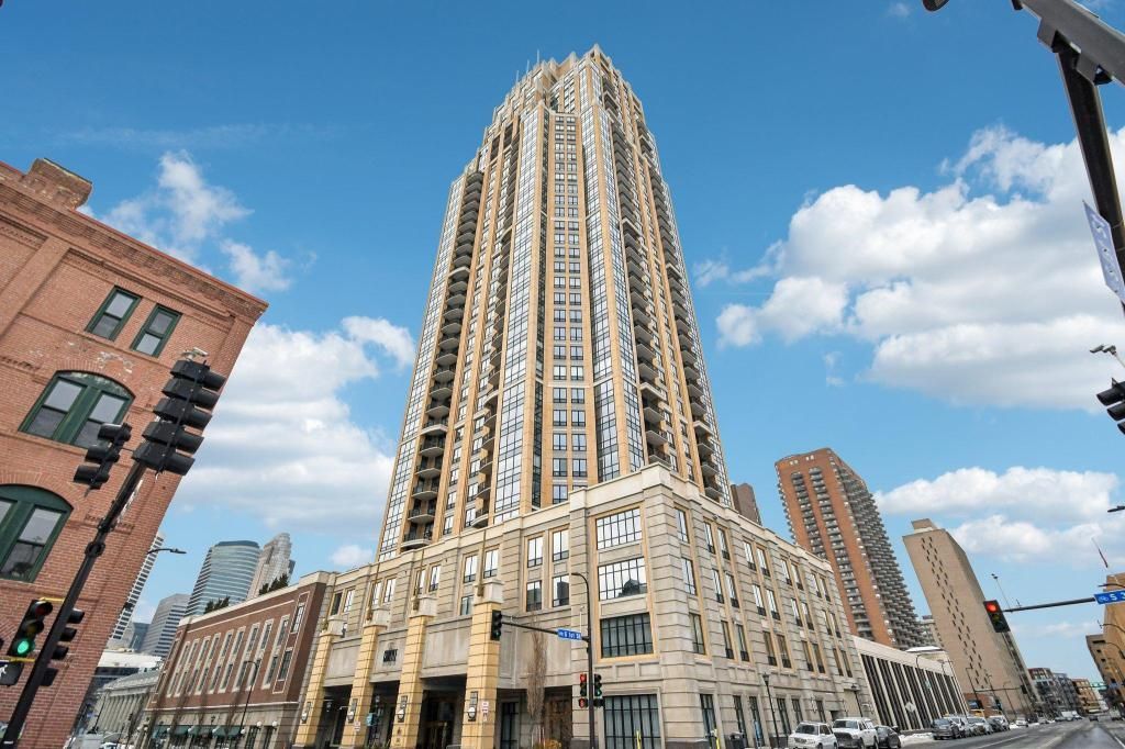 Tall beige skyscraper against a blue sky with clouds, viewed from street level in a city intersection