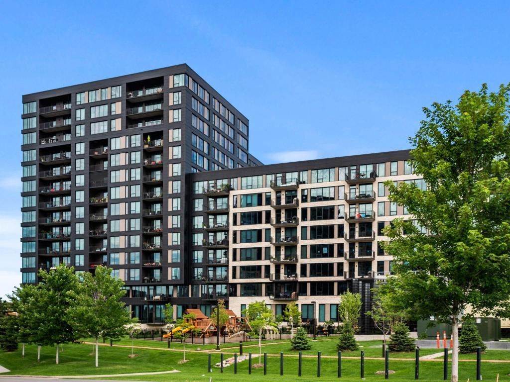 Modern apartment buildings beside a green park with trees under a clear blue sky