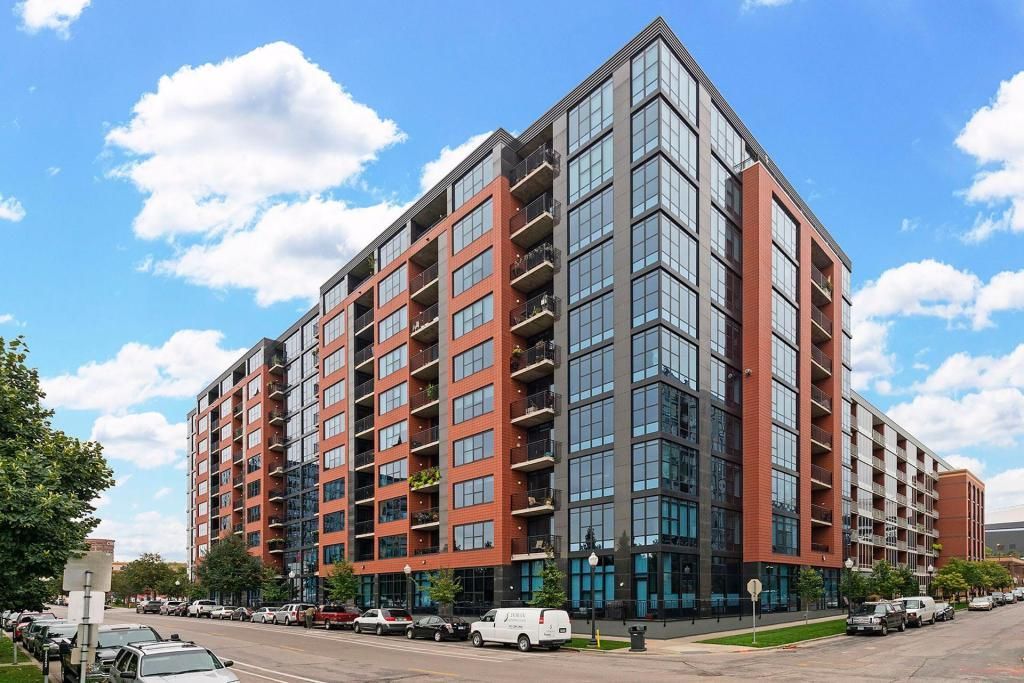 Modern red-brick apartment building with glass corner facade on a city street under a blue sky