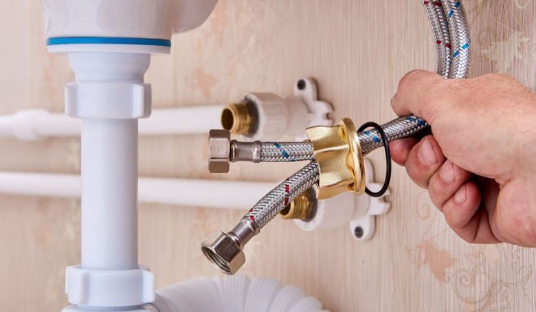 Plumber connecting chrome pipes under a sink with a wrench on a wooden wall panel