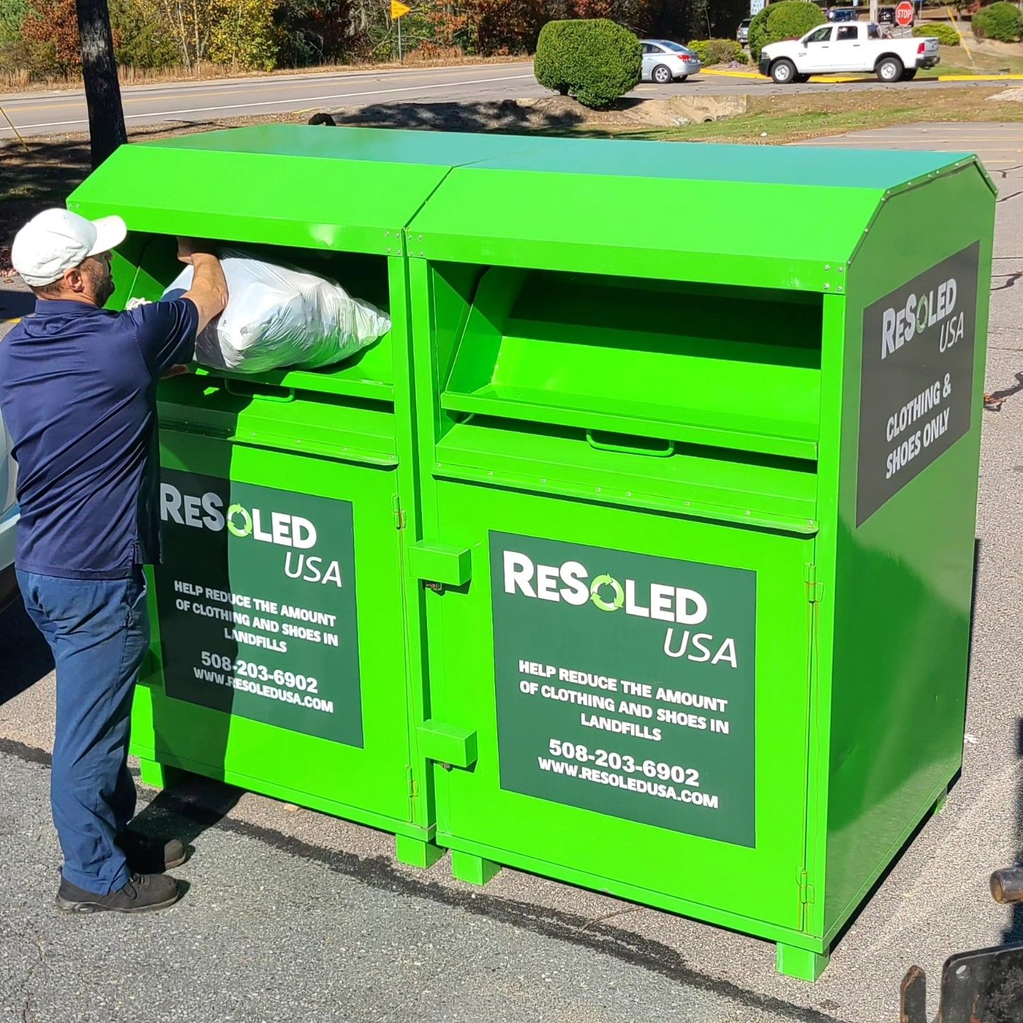 A man is putting a pillow into a green recycling bin.