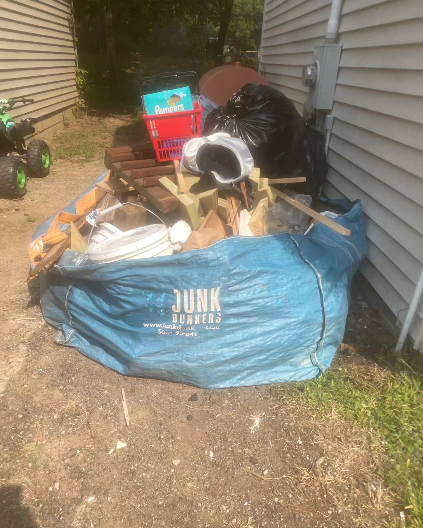 A blue bag filled with junk is sitting in front of a house.