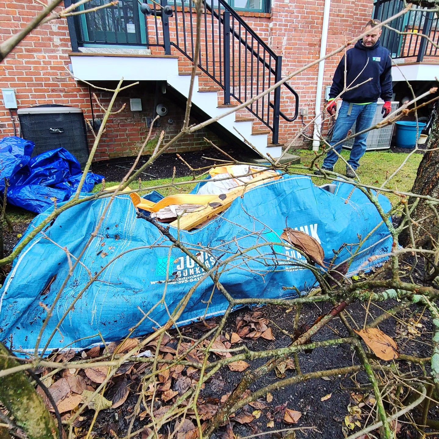 A man is standing in front of a brick house with a blue tarp on the ground