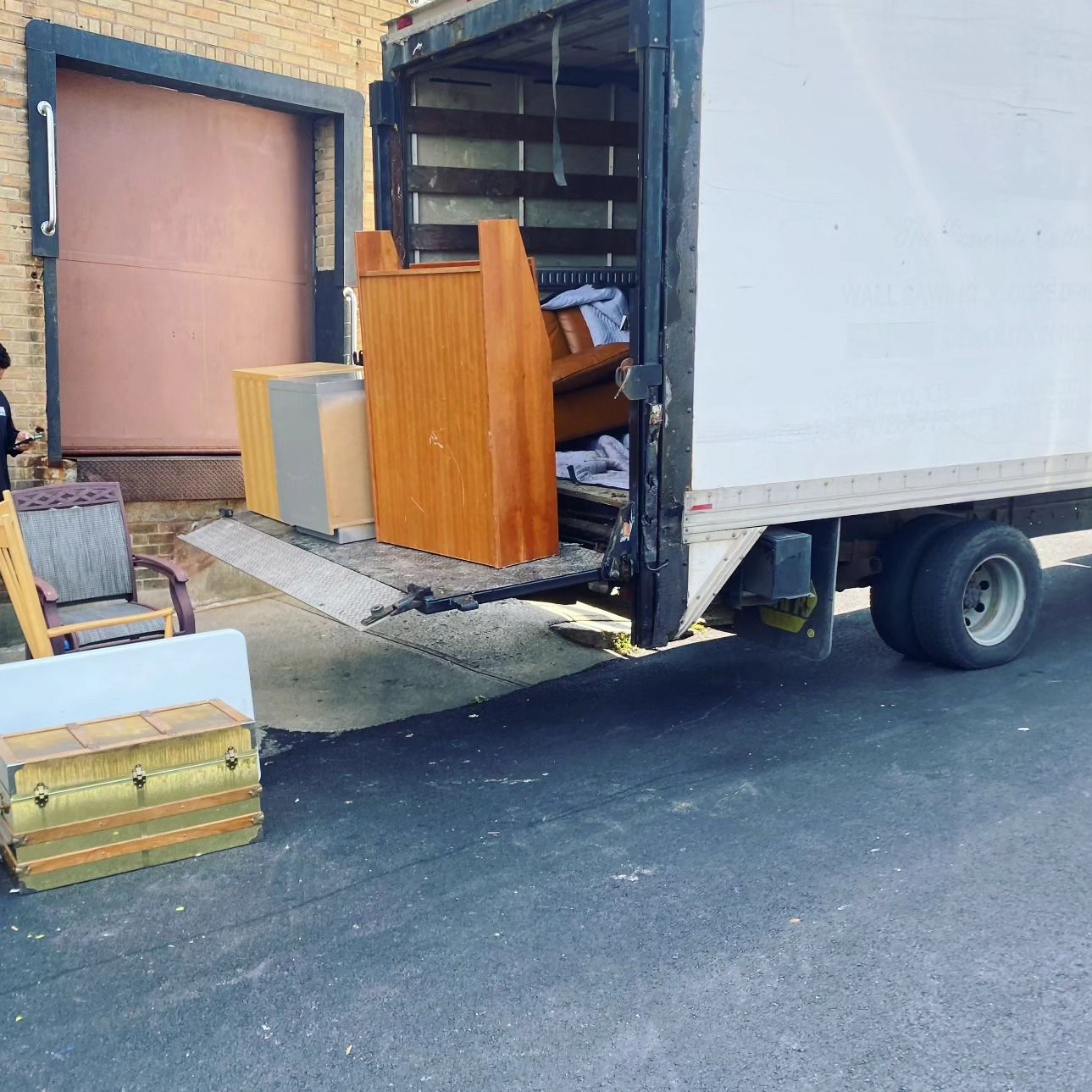 A white truck is parked in front of a brick building filled with furniture.