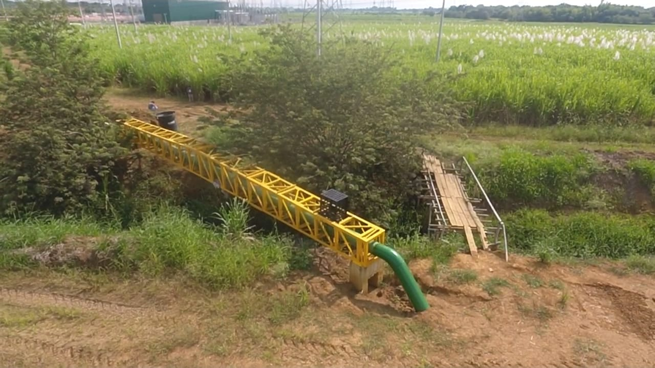 Un puente amarillo está en el medio de un campo al lado de una tubería verde.
