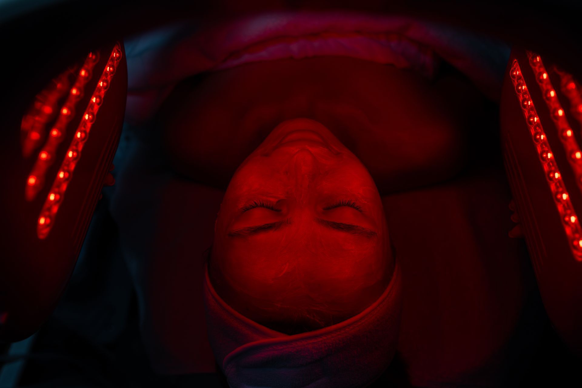 Person receiving a facial treatment with a glowing device on the neck and jawline