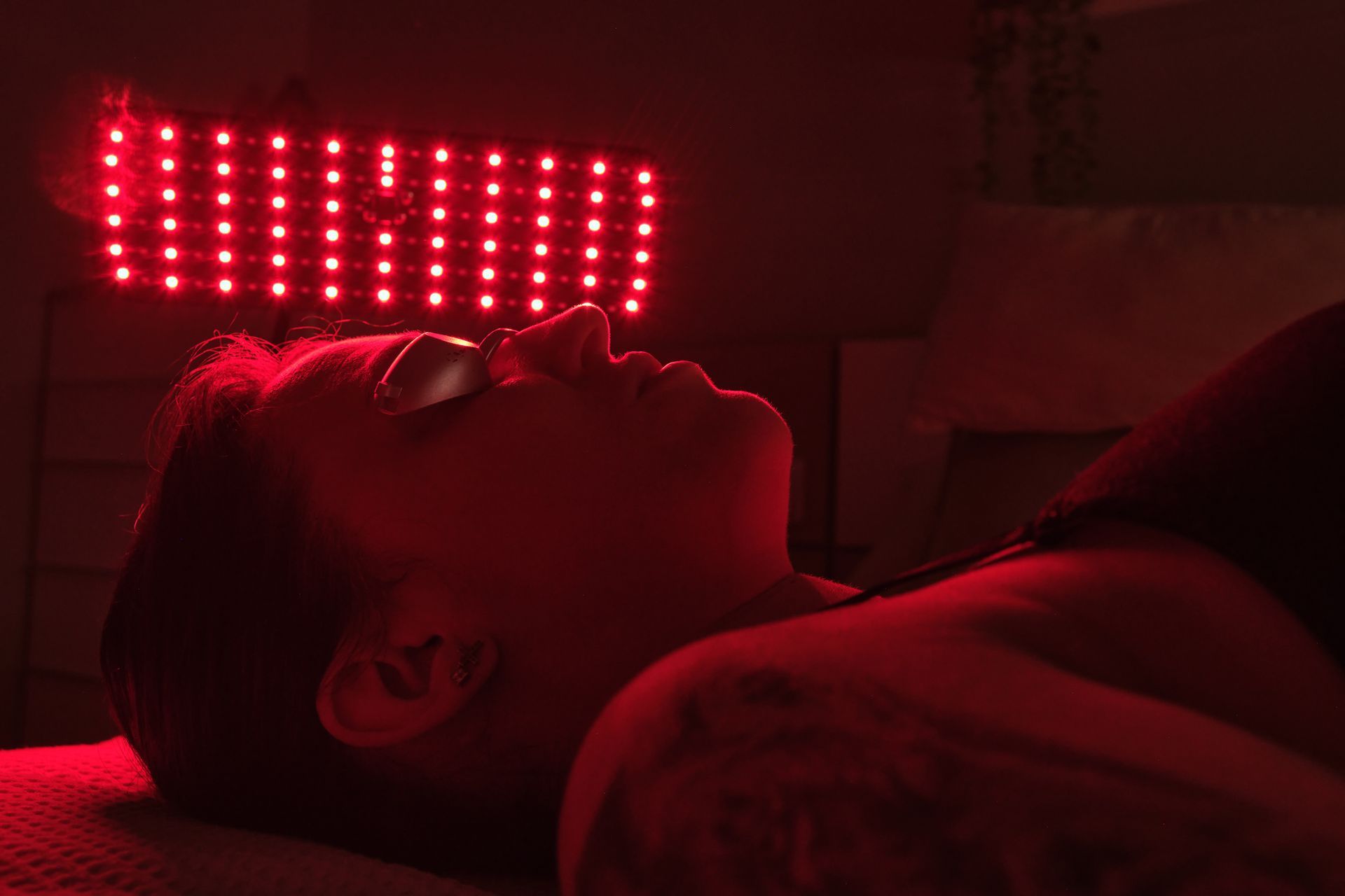 Person lying under a red light therapy panel, wearing glasses, in a relaxed pose