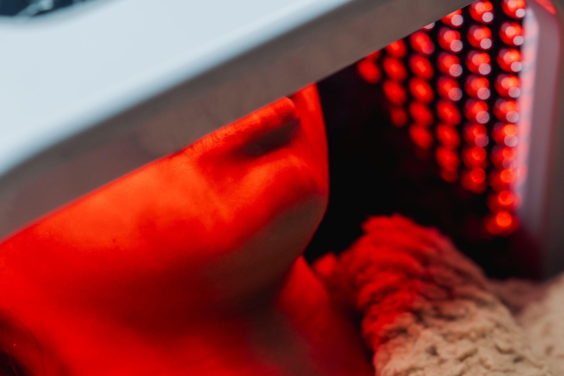 Close-up of a face lit by red LED light near a glowing device panel