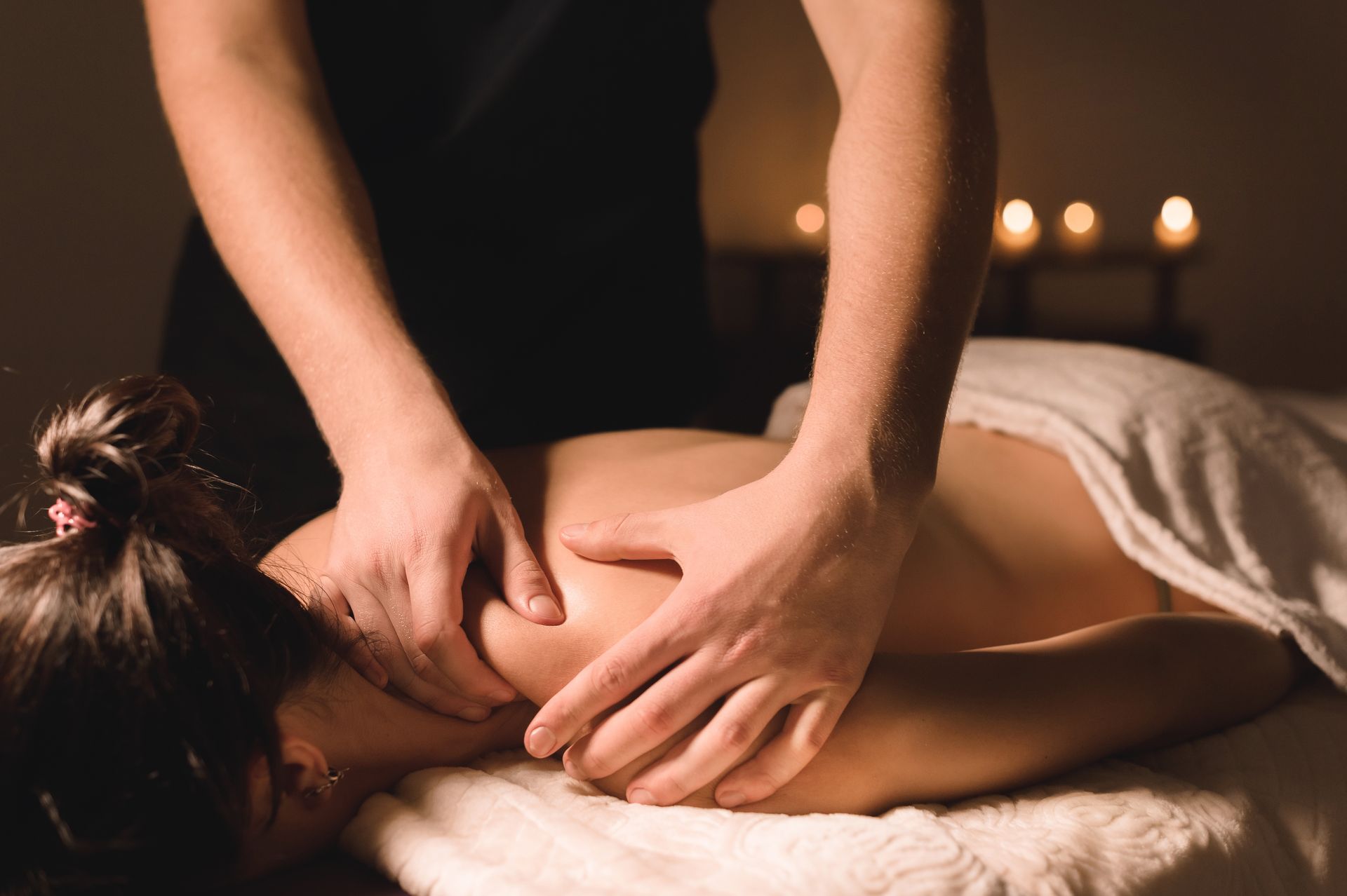 Person receiving a back massage in a dimly lit spa with candles nearby