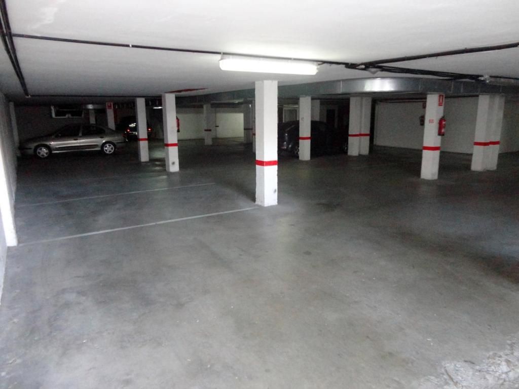 Garaje subterráneo vacío con pilares de hormigón y un coche aparcado a la izquierda.