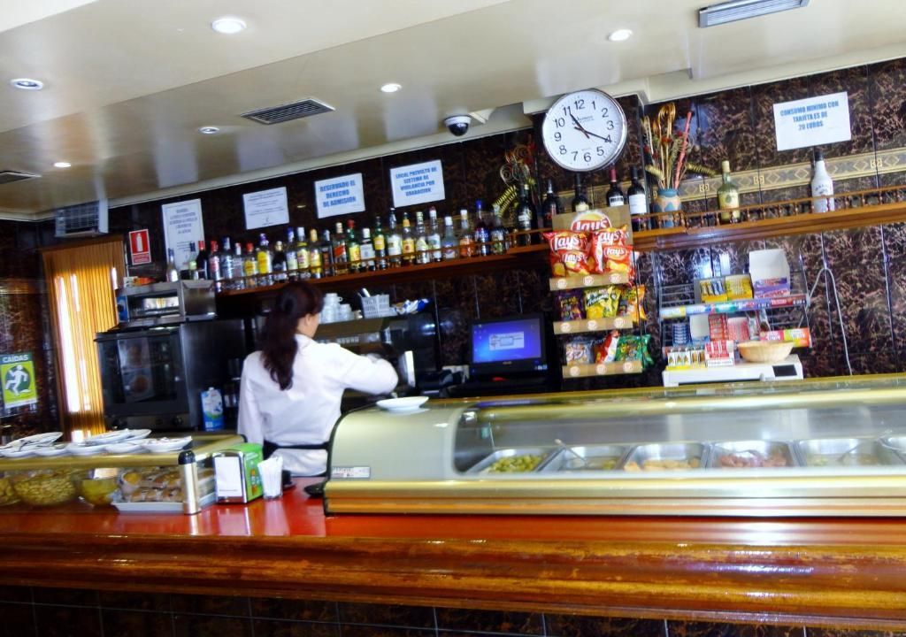 Un camarero detrás de la barra con botellas, grifos y un reloj de pared en un pub acogedor.