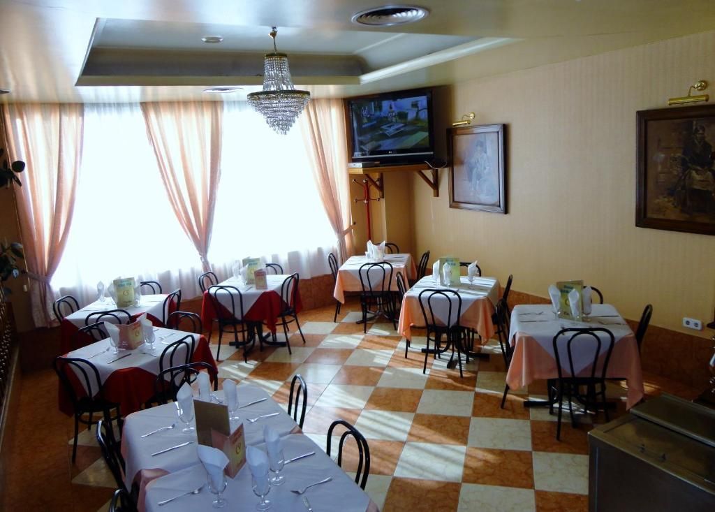 Comedor vacío de un restaurante con suelo de baldosas a cuadros, manteles blancos y televisor montado en la pared.