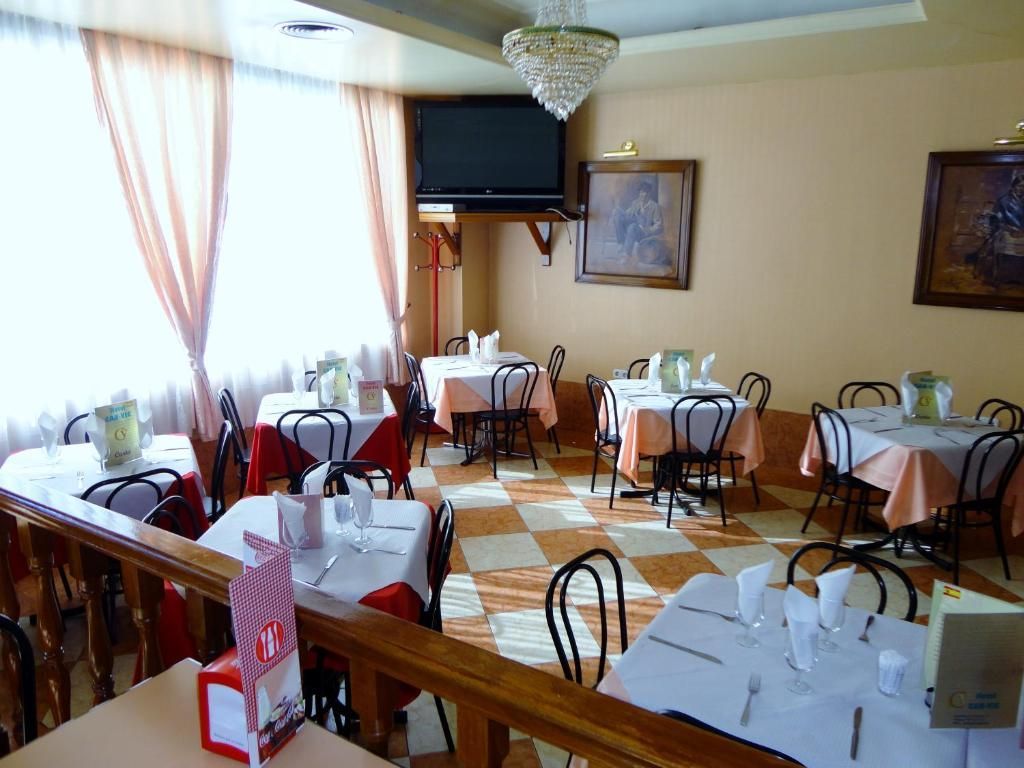 Comedor de un restaurante con manteles blancos, sillas negras y luz solar que se filtra a través de cortinas transparentes.