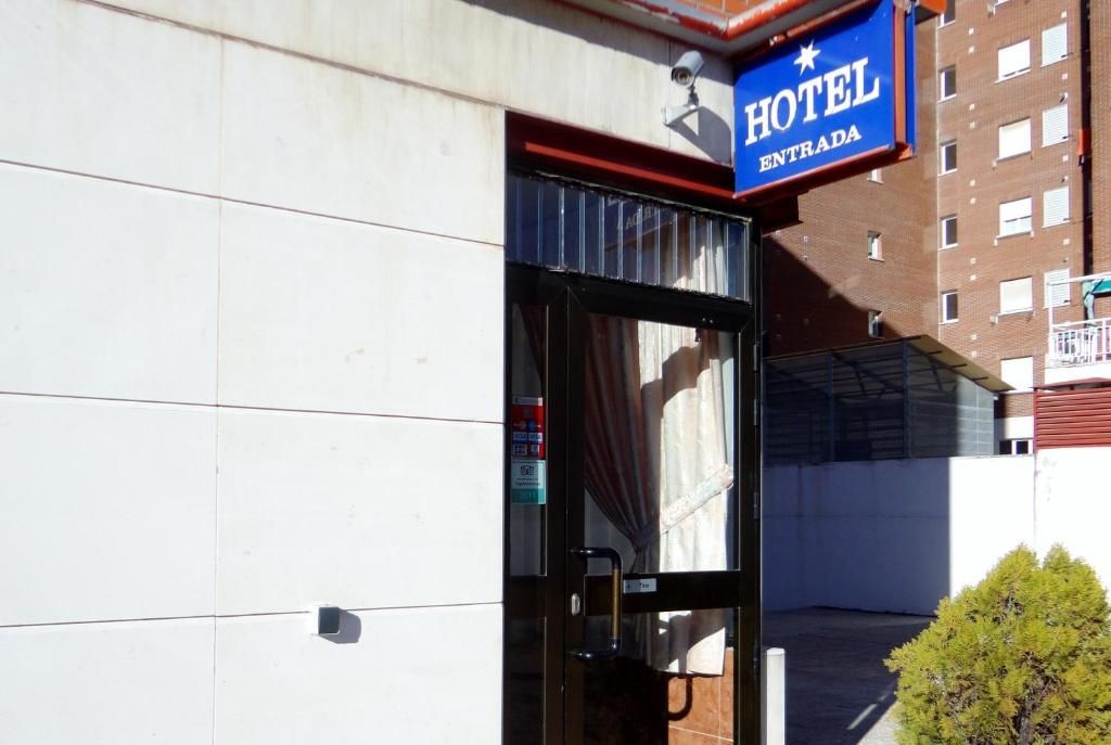 Entrada del hotel con letrero azul y puerta de cristal junto a una pared blanca.