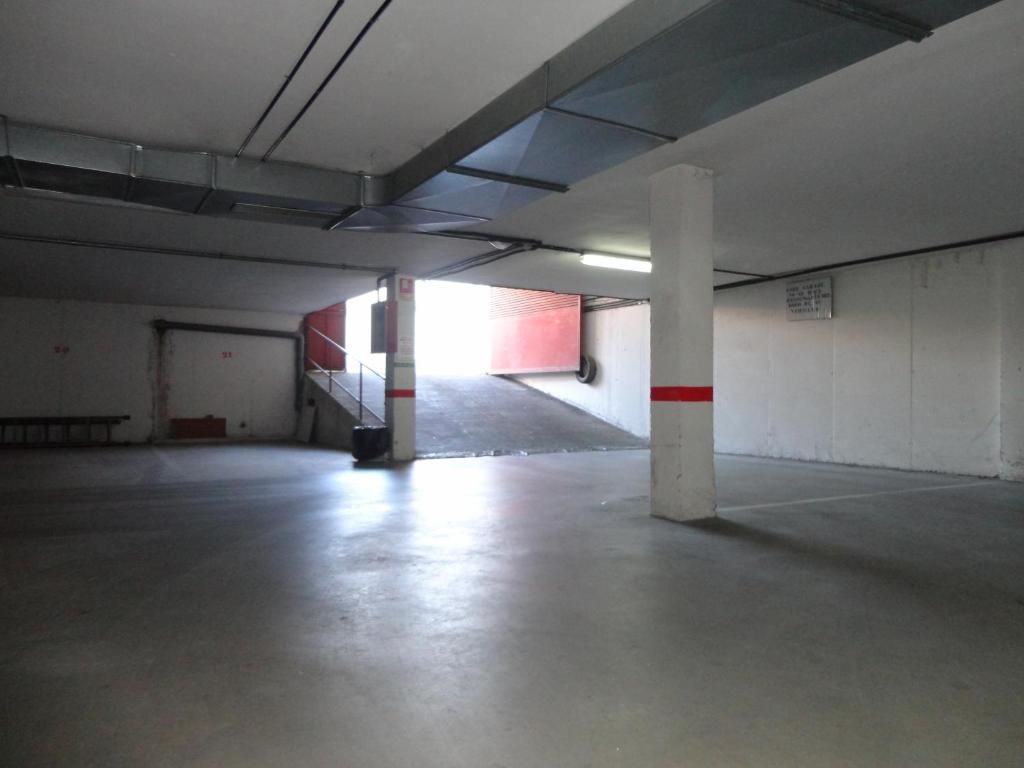 Garaje cubierto vacío con pilares de hormigón y entrada abierta iluminada en rojo.