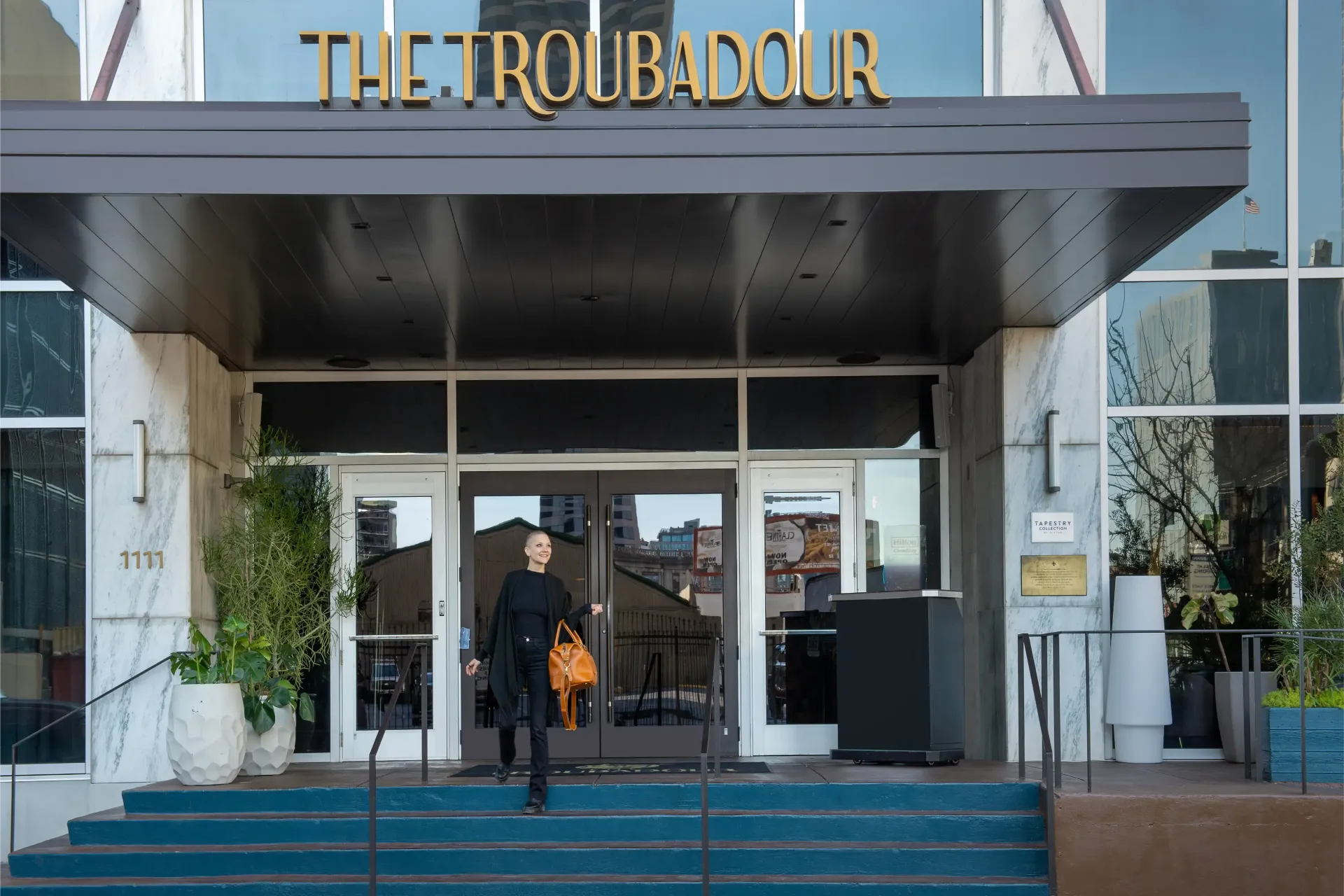 A woman is standing in front of the troubadour hotel an independent hotel New Orleans Louisiana.