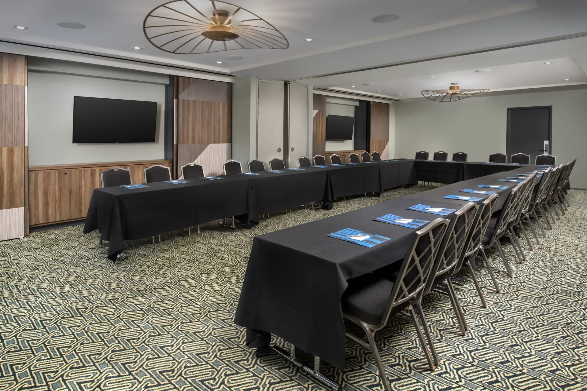 A conference room with long tables and chairs and a flat screen tv.