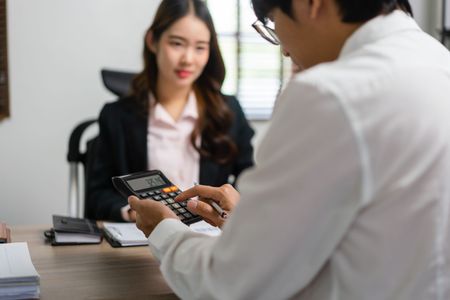 Two people discuss a document at a desk while one uses a calculator