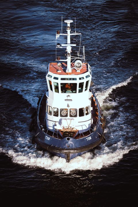 Small white tugboat with black hull cutting through dark water, viewed from above
