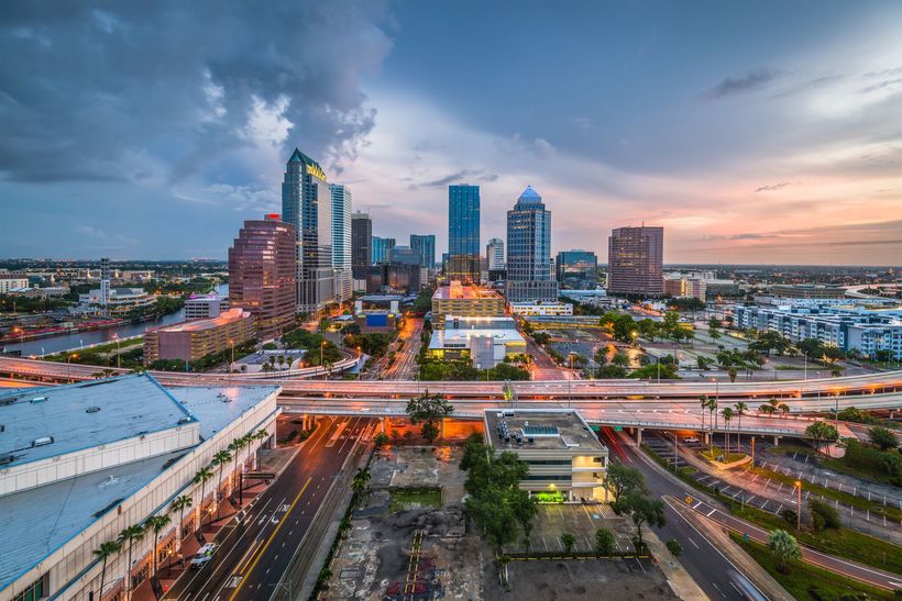 City skyline at dusk with elevated highway, traffic light trails, and a cloudy sunset sky