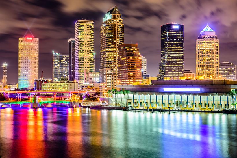 Night city skyline with brightly lit skyscrapers reflected in colorful water at dusk