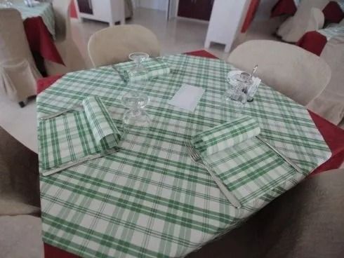 In una sala da pranzo, un tavolo rotondo apparecchiato con tovaglie a quadri verdi e tovaglioli piegati.