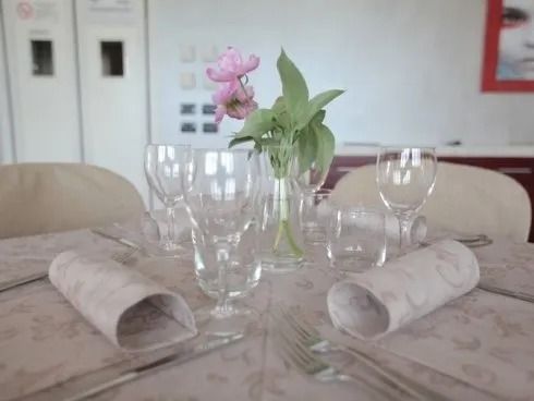 Apparecchiare la tavola con bicchieri, tovaglioli arrotolati e un vaso di fiori