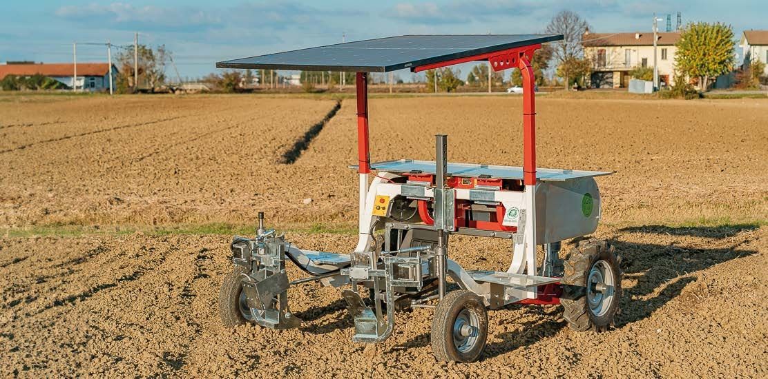 Un robot agricolo a energia solare lavora in un campo aperto e arato, sotto un cielo sereno.