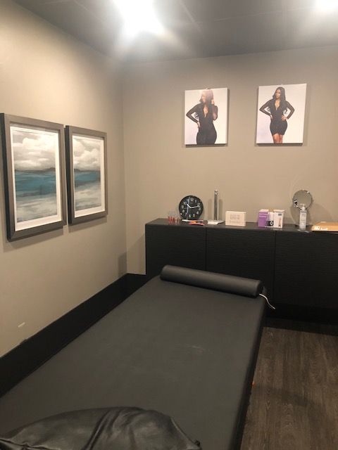 Massage room with a black massage table, artwork on walls, and black storage cabinets.