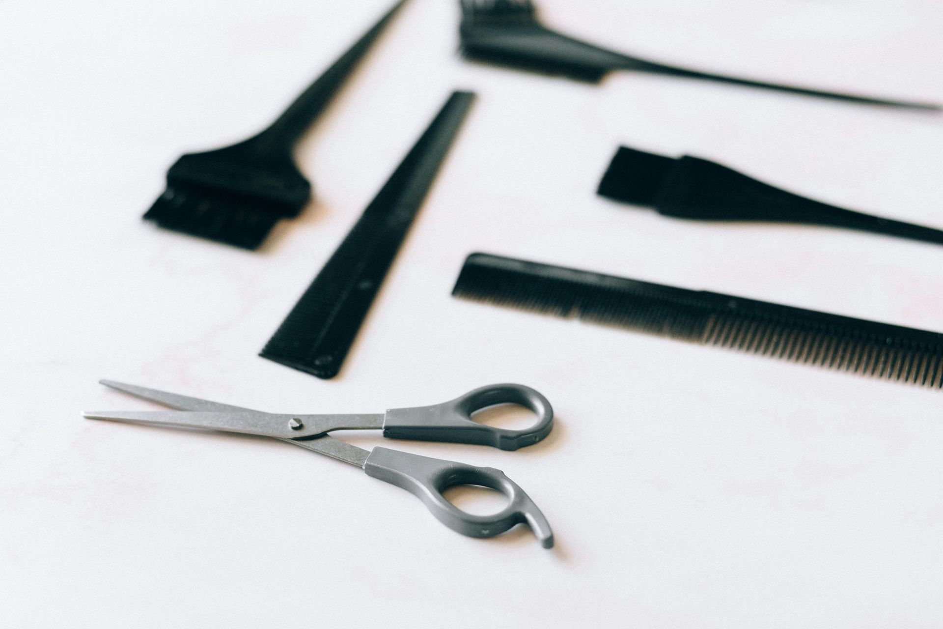 Black hair styling tools including scissors, brushes, and combs on a white surface.