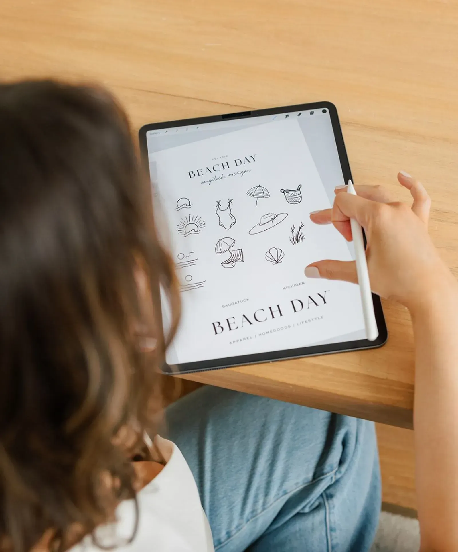 A person uses a stylus on a tablet screen displaying a collection of beach-themed illustrations and the text