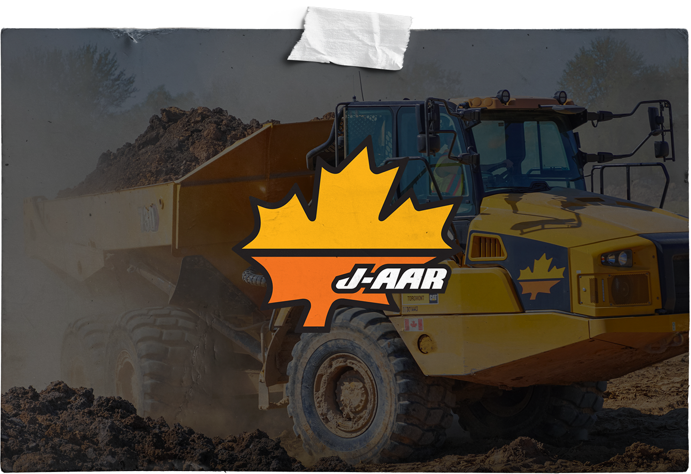 A yellow dump truck with a maple leaf on the side is driving down a dirt road.