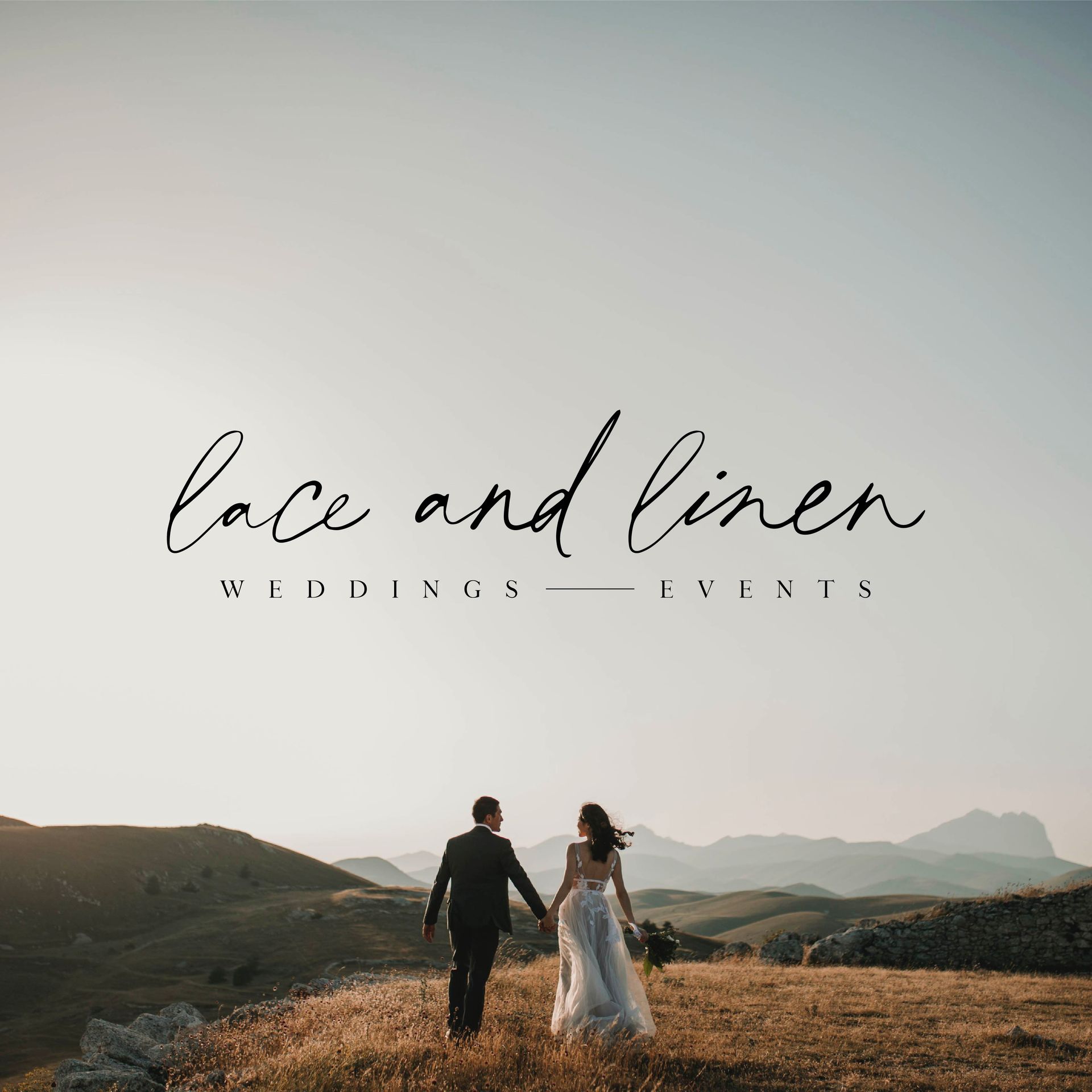 A bride and groom are walking on top of a hill holding hands.