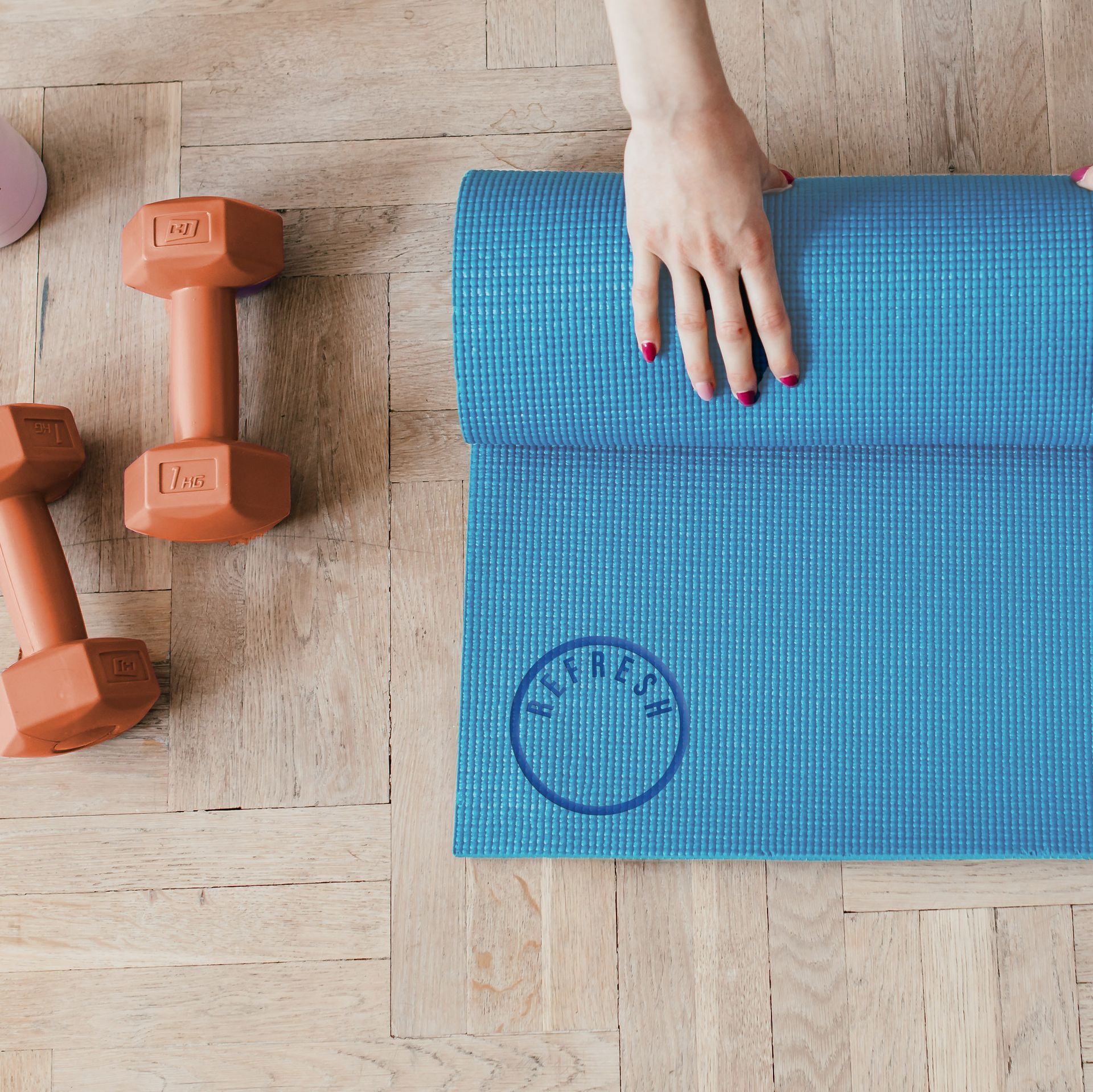 A woman 's hand rests on a blue yoga mat next to dumbbells.