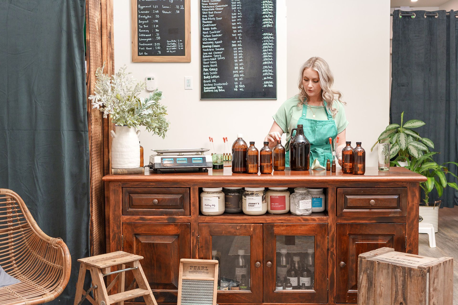 A woman in an apron is standing behind a counter filled with bottles.
