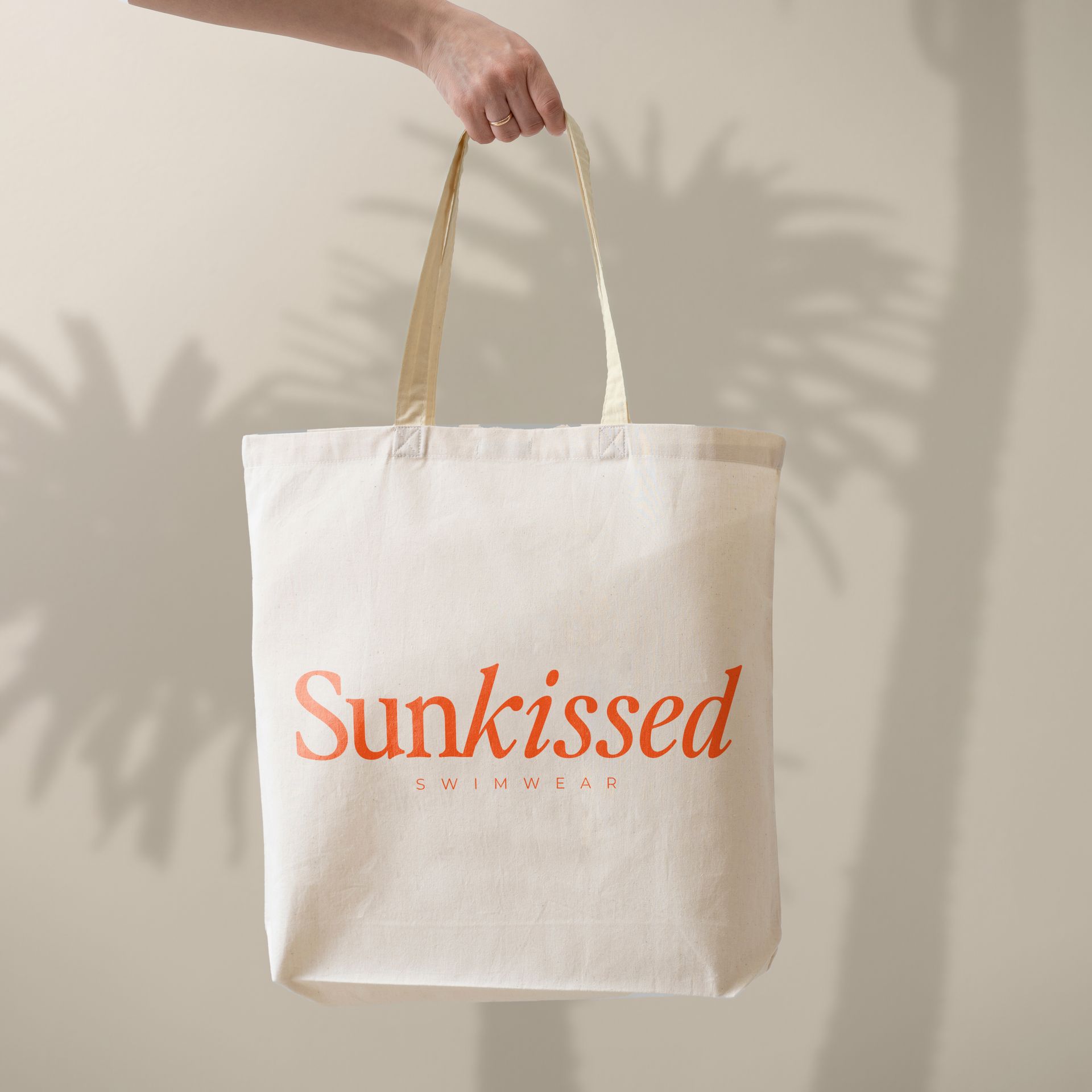 A person is holding a white tote bag that says sunkissed
