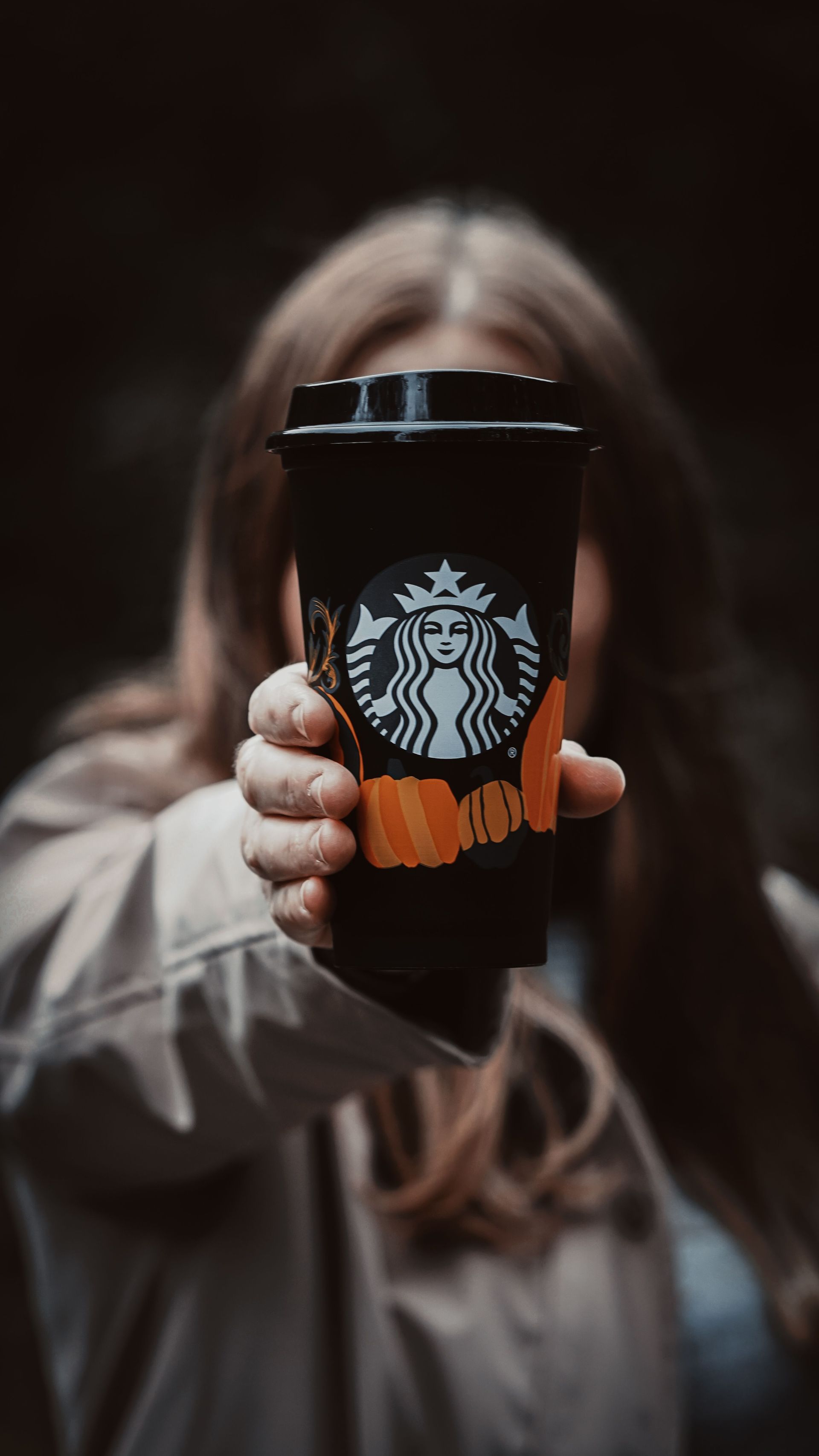 Person holding a black Starbucks cup toward the camera against a dark blurred background.