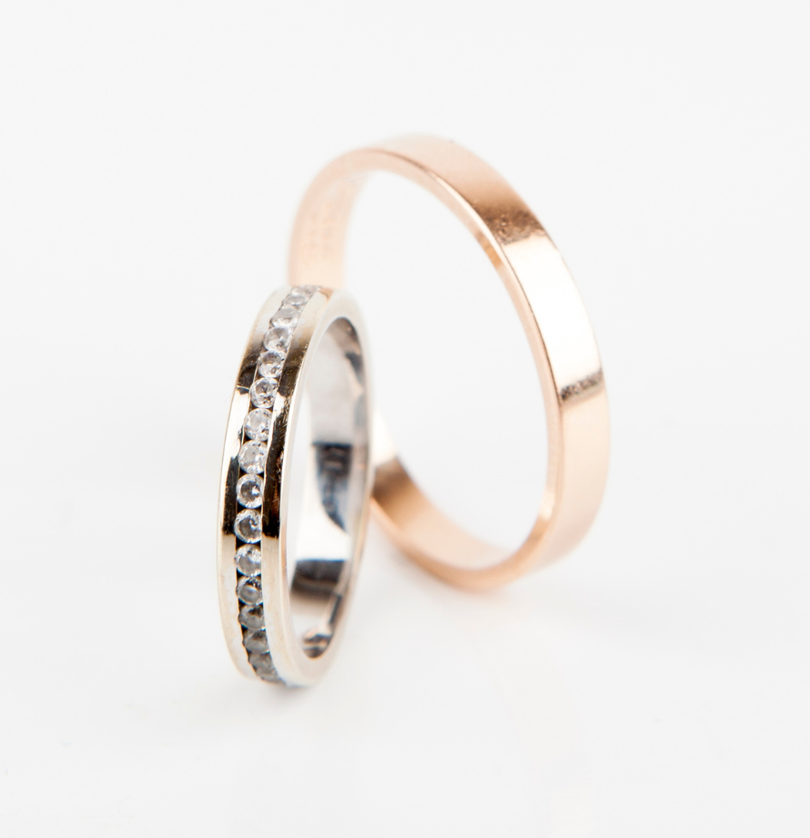 Two metallic wedding bands, one silver with diamonds and one rose gold, on a white background