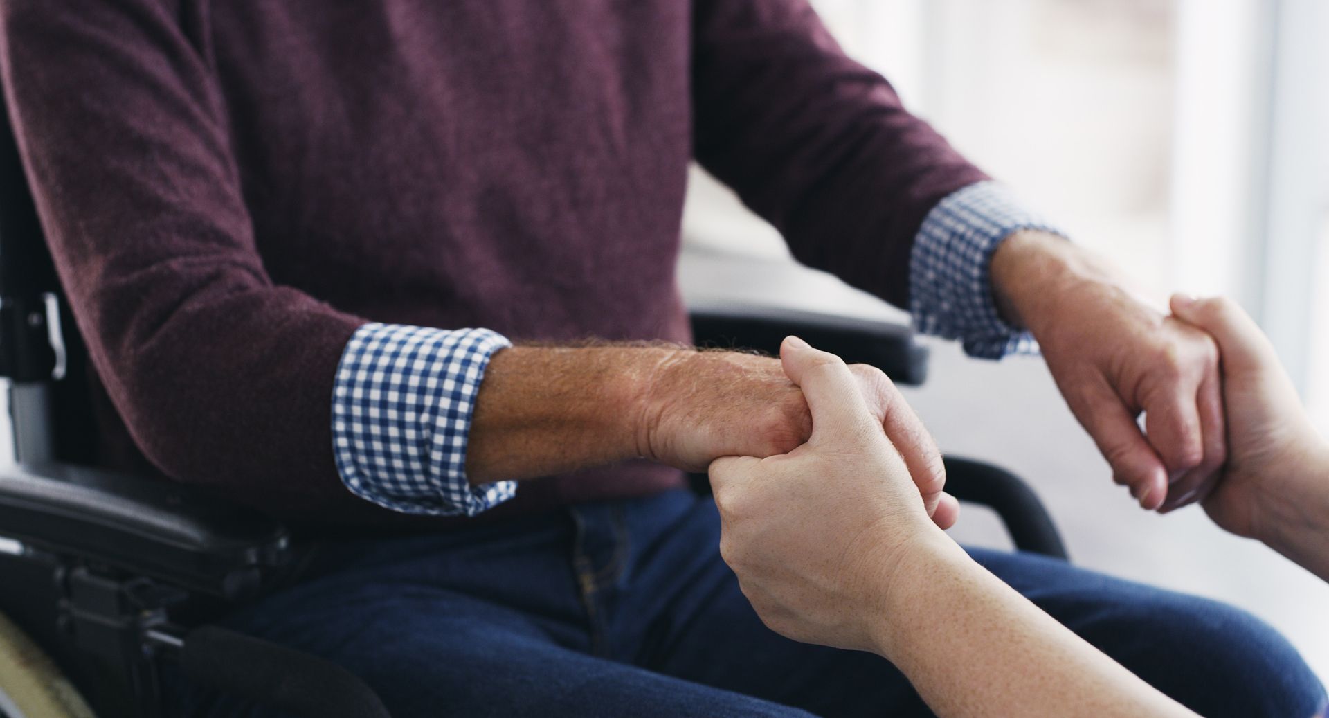A person is holding the hand of a man in a wheelchair.