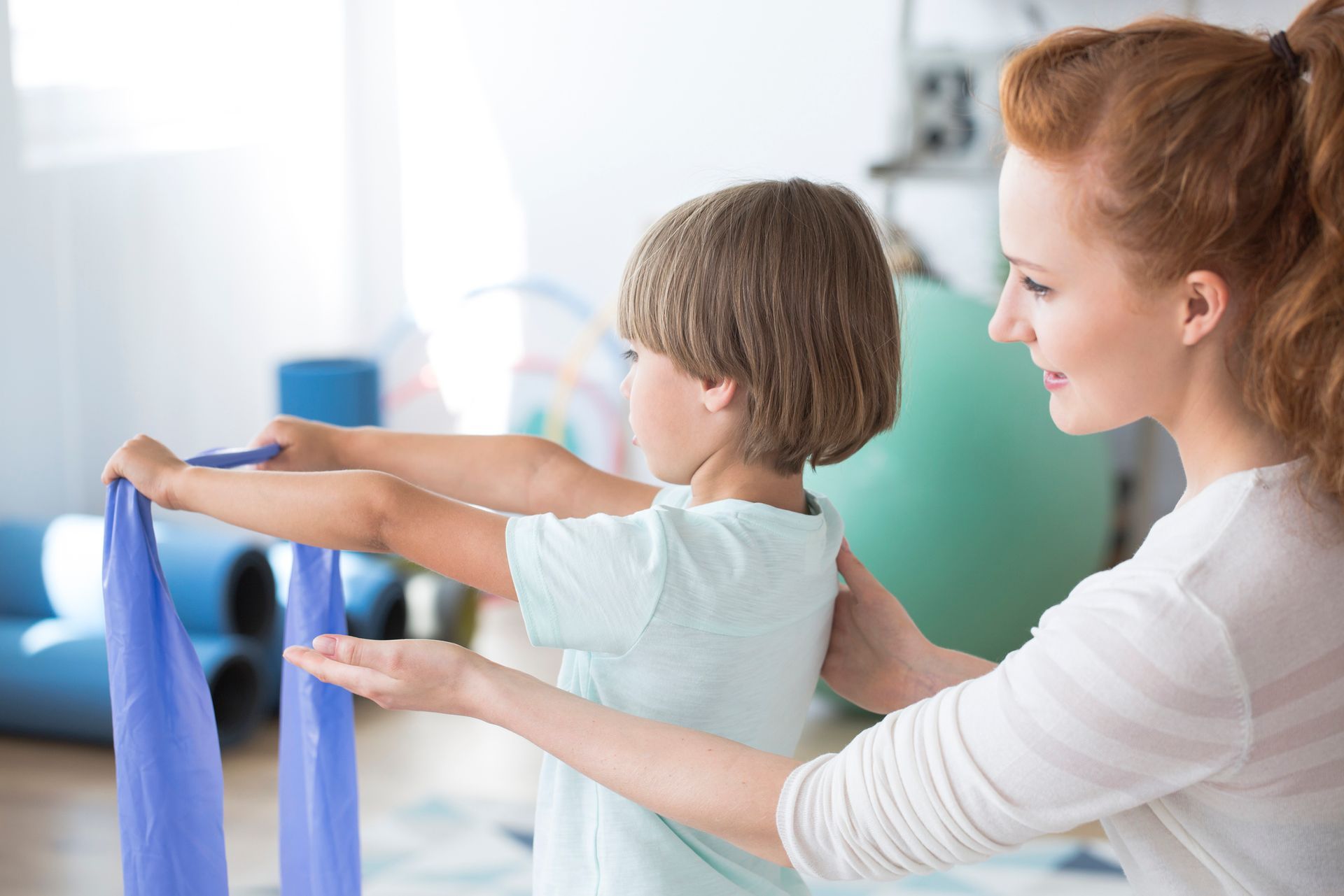 A woman is helping a young boy with a resistance band.