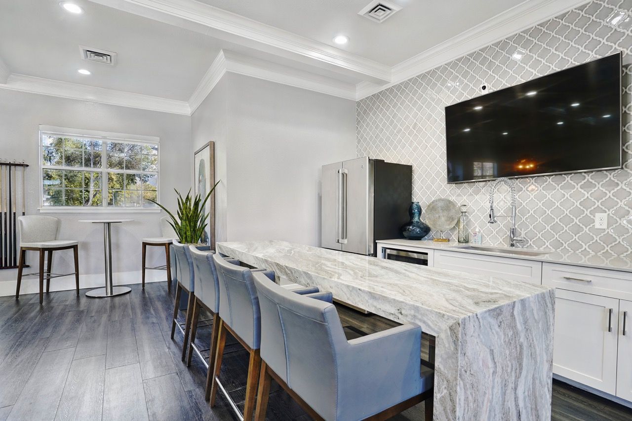Modern apartment kitchen with marble island, seating, stainless fridge, and wall-mounted TV at Preston Hollow in Millcreek, UT.