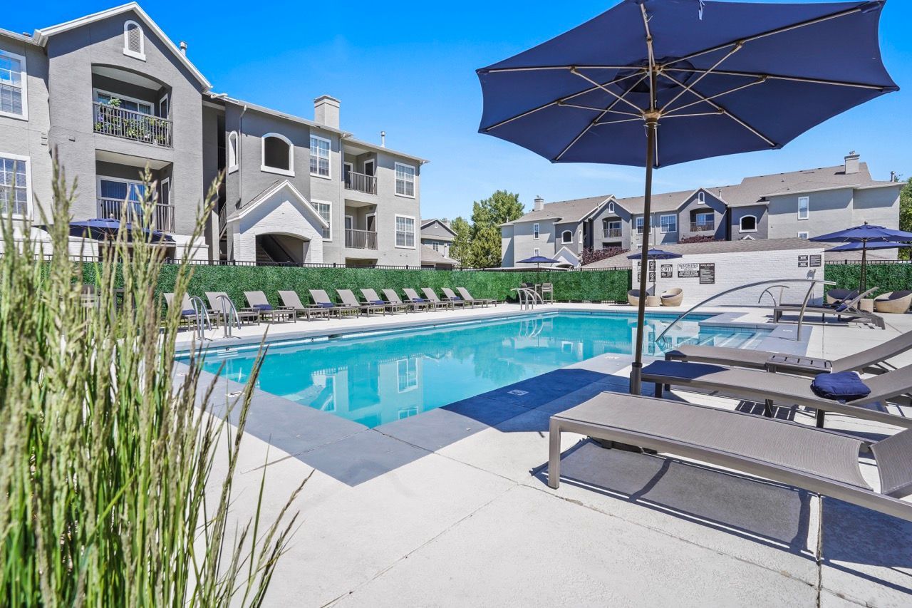 Outdoor pool area at a multi-building apartment community with lounge chairs and blue umbrellas at Preston Hollow in Millcreek, UT.