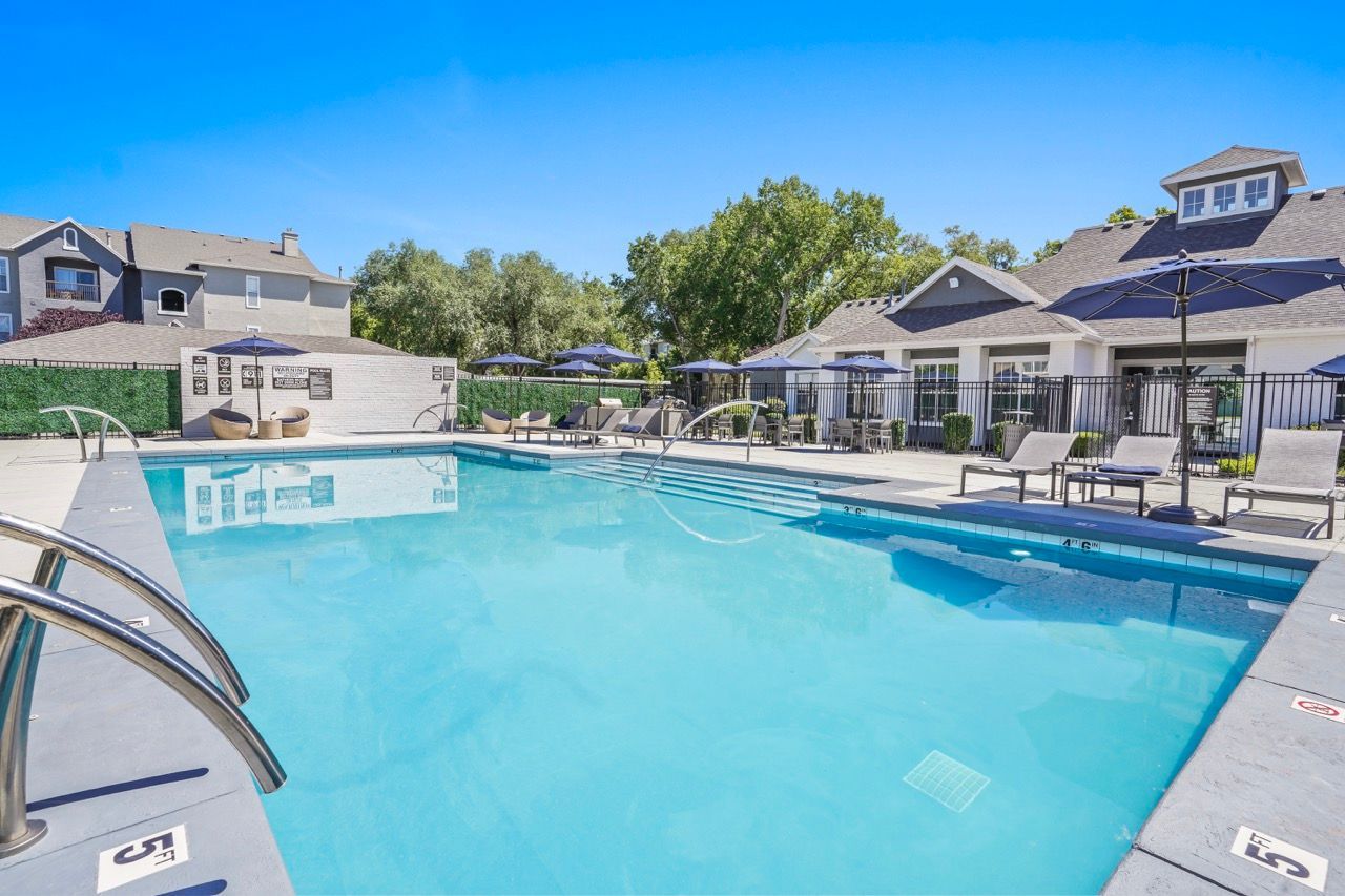 Outdoor community pool with lounge chairs and umbrellas, surrounded by apartment buildings at Preston Hollow in Millcreek, UT.
