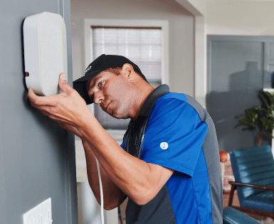 Technician in blue shirt repairing a wall-mounted device indoors