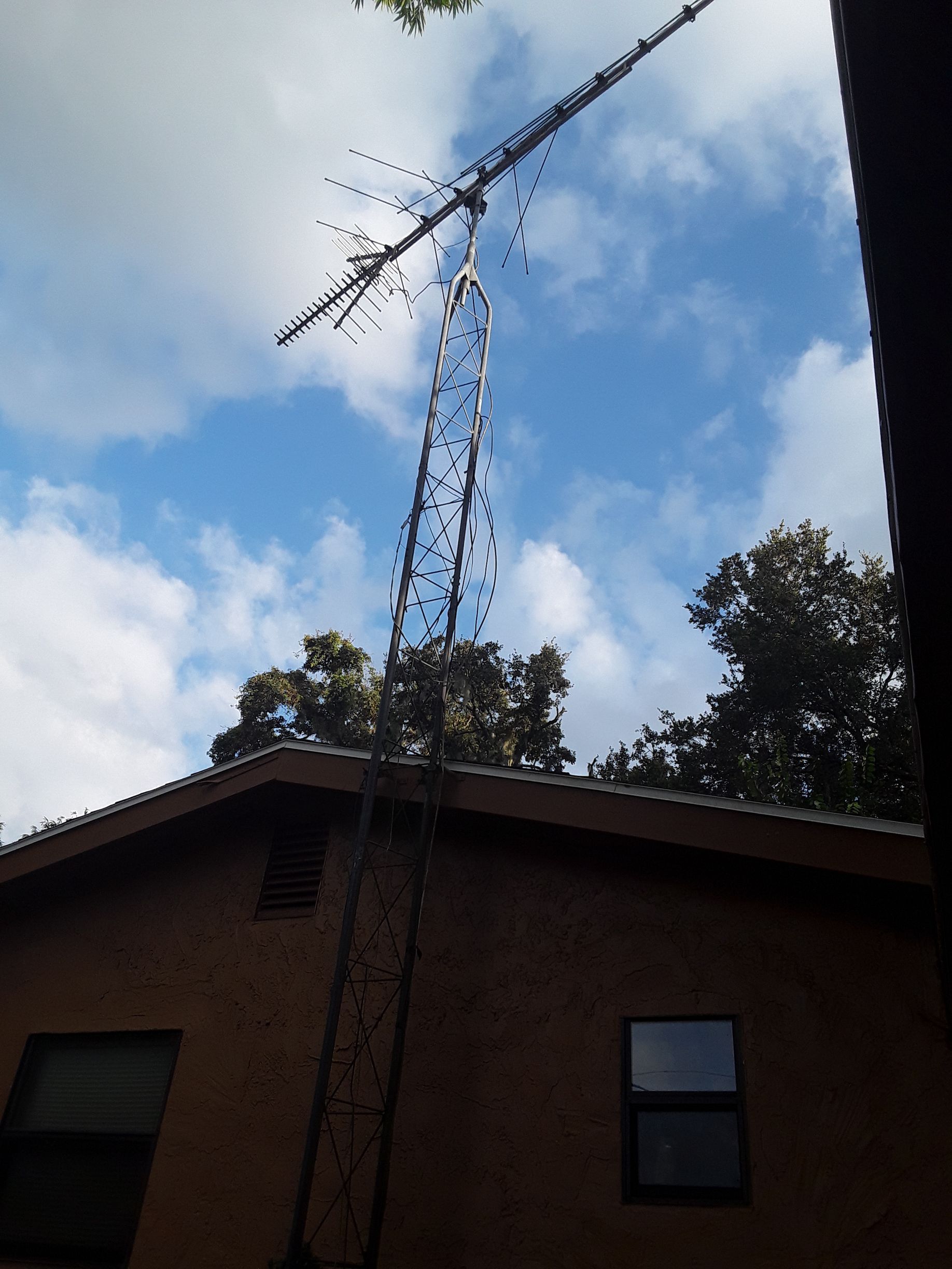A tall radio tower with antennas atop a building, against a cloudy blue sky.