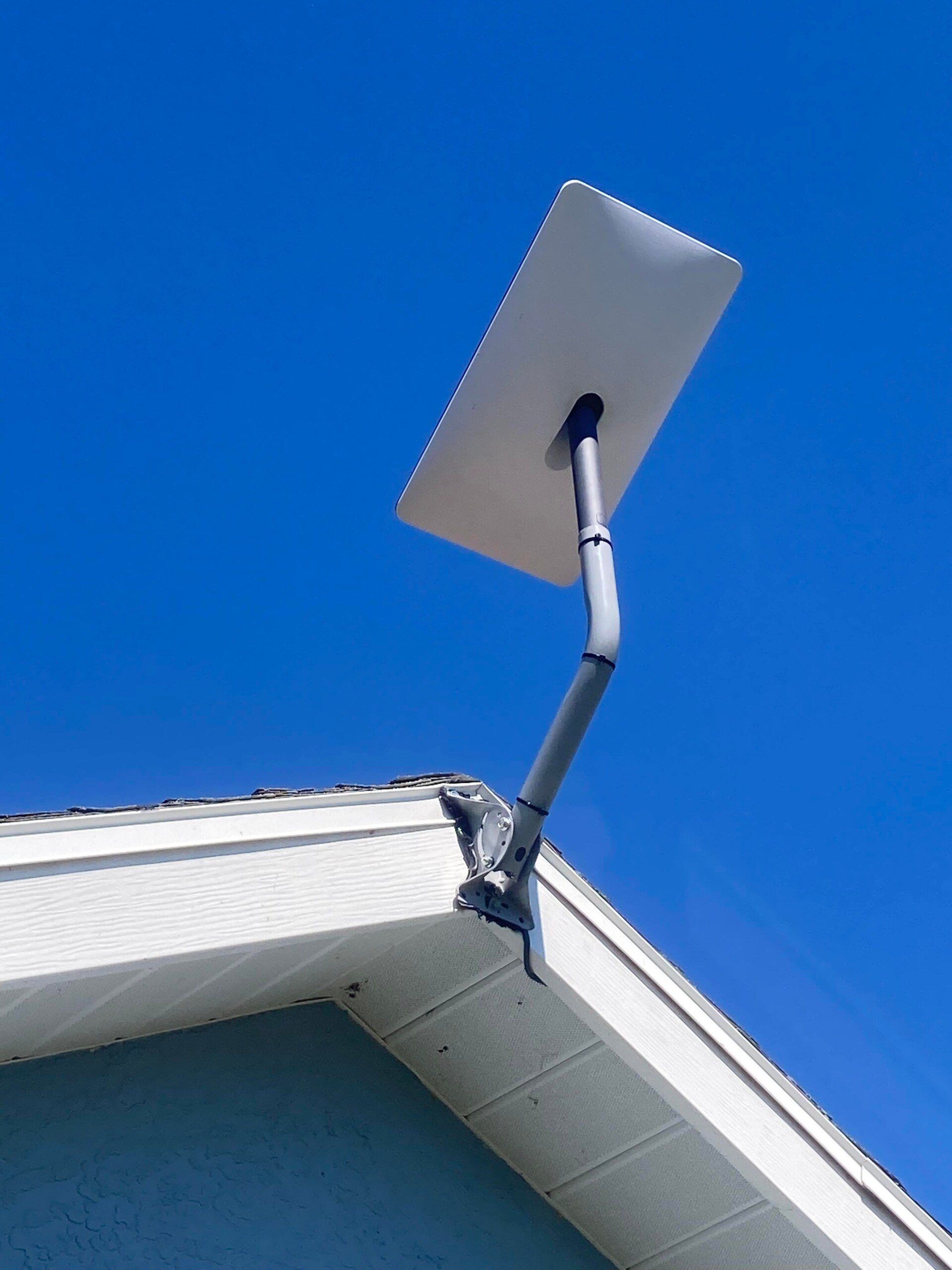White satellite dish mounted on a house roof against a blue sky.