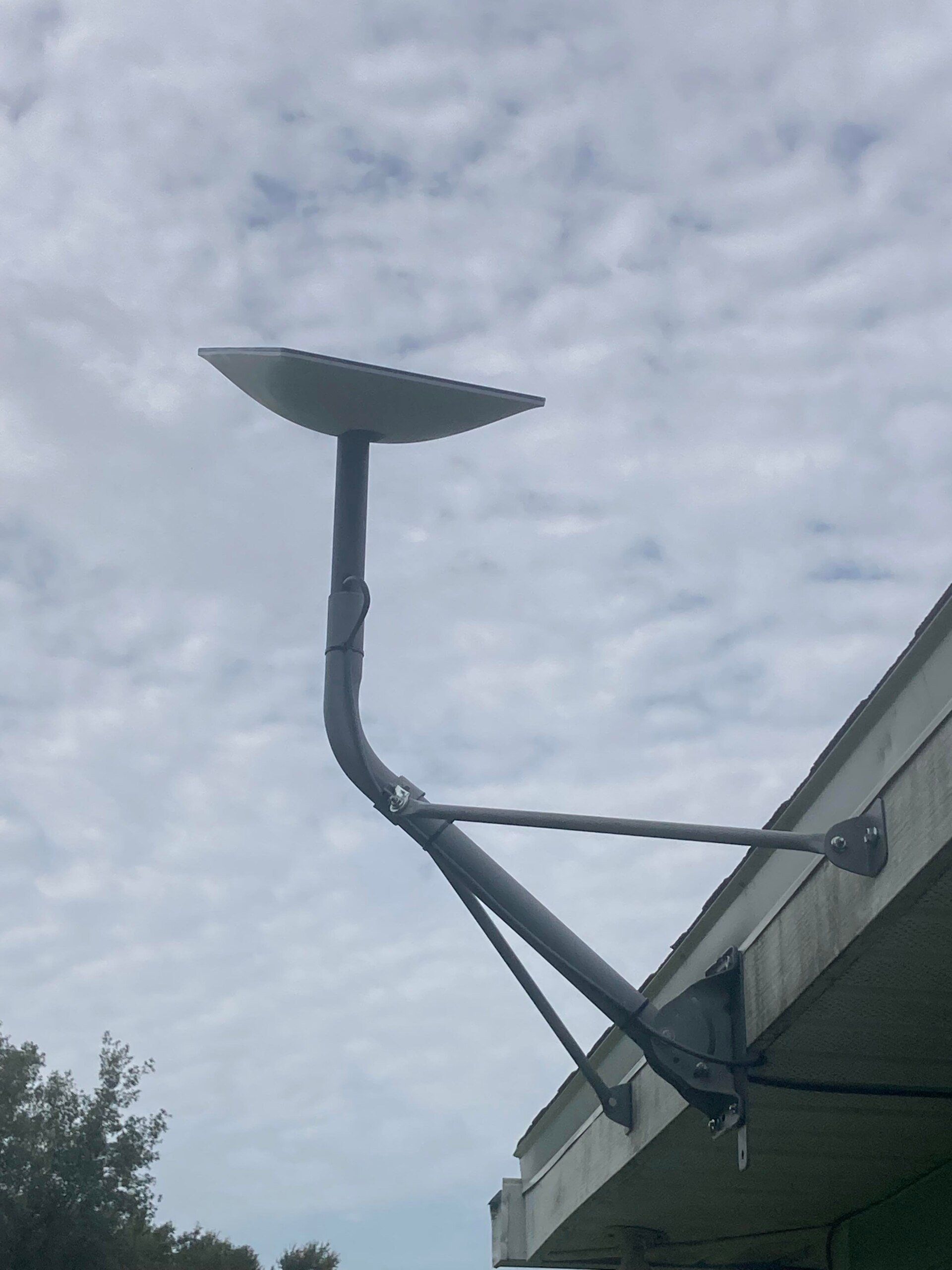 Satellite dish mounted on a building's roof with cloudy sky in the background.