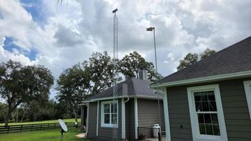 Two tall poles with antennas stand near a house. Overcast sky.