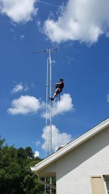 Person climbing a tall antenna tower with clear blue sky and fluffy clouds.