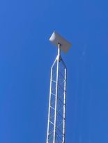 Tall, silver cellular tower against a clear blue sky. A rectangular antenna is at the top.